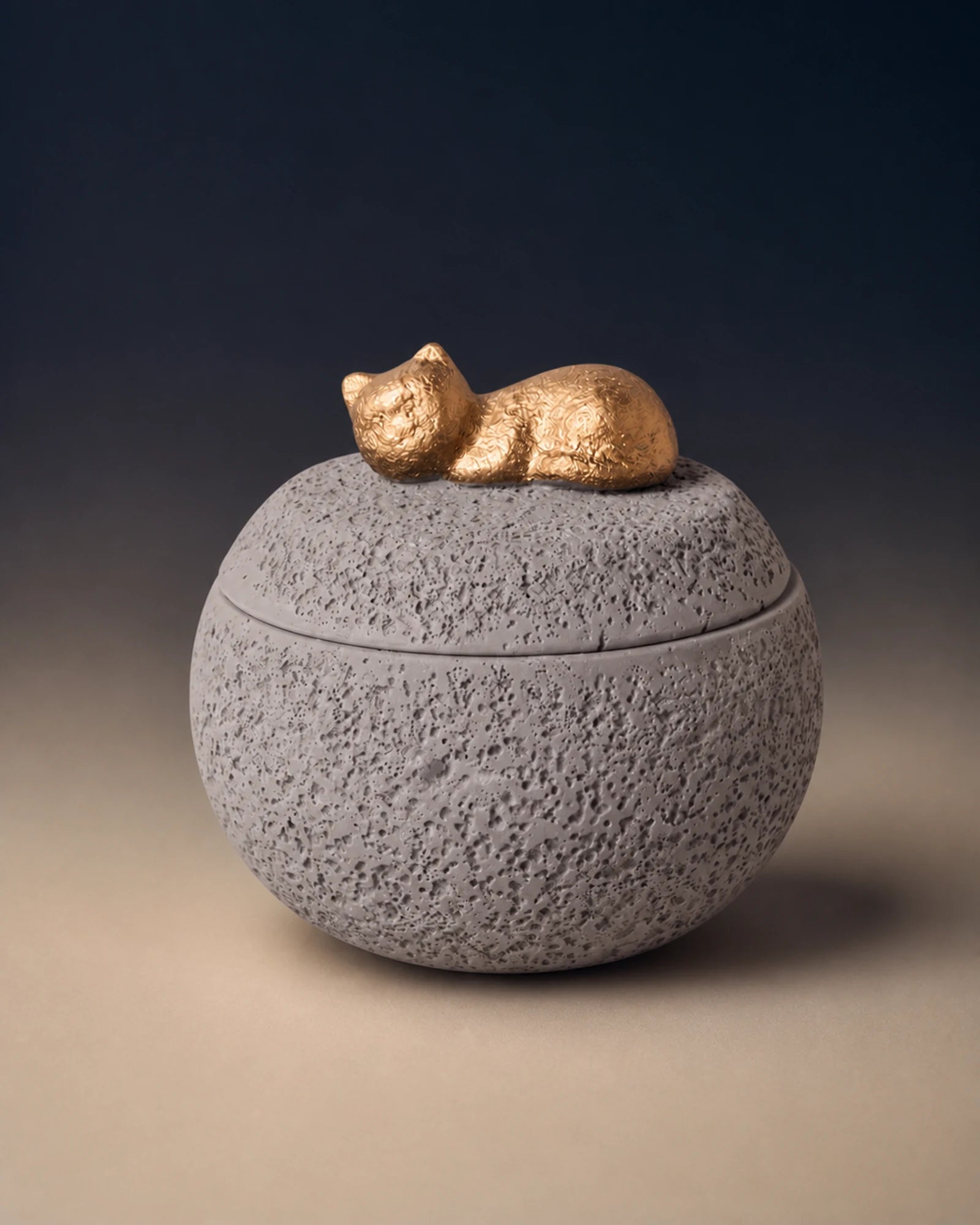 Gray cement-textured memorial urn topped with a small gold sleeping cat