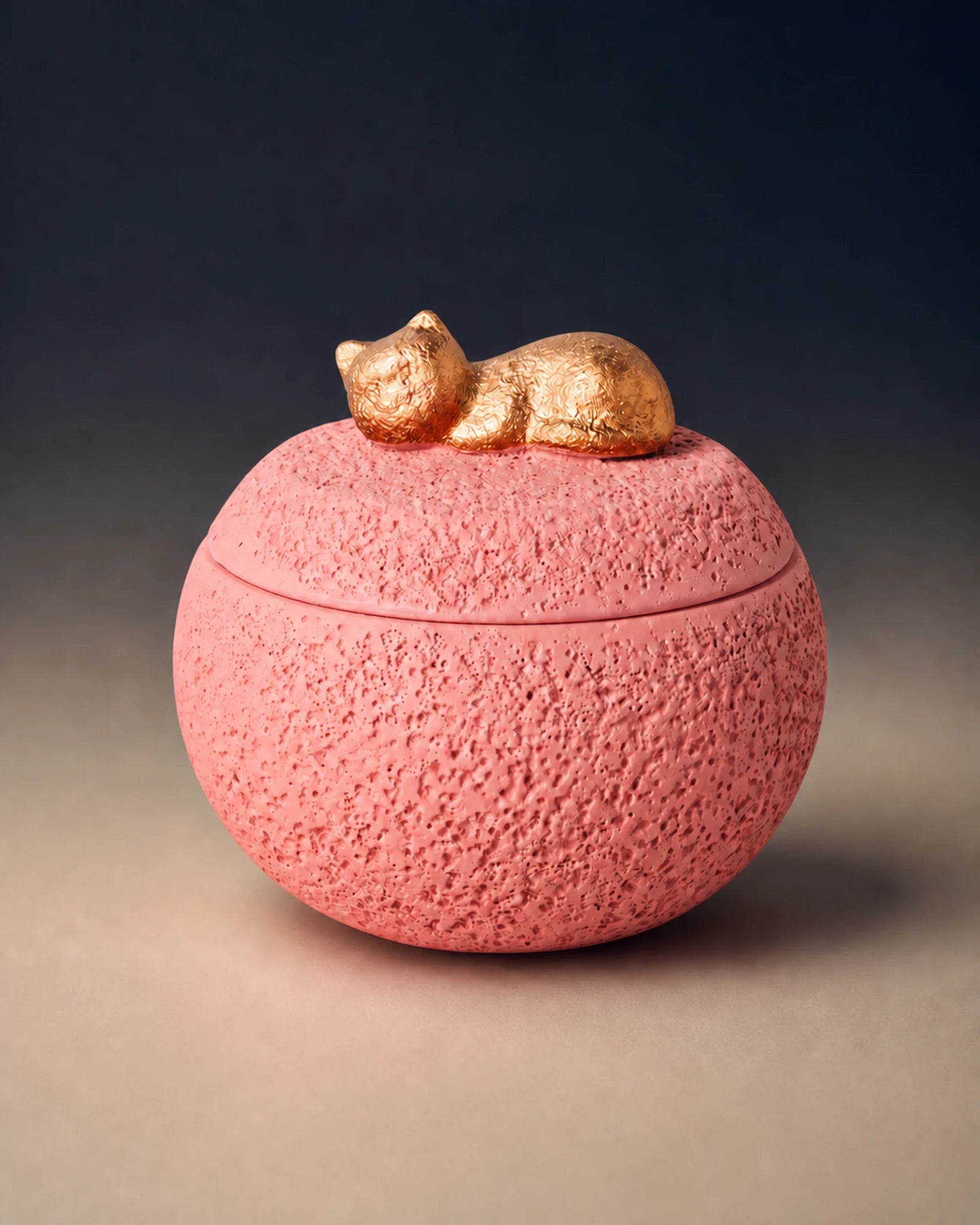 Pink cement-textured memorial urn topped with a small gold sleeping cat